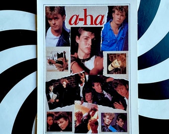 Può includere: Un foglio di adesivi vintage degli a-ha con più immagini dei membri della band. Il nome della band, "a-ha", è in rosso. Il foglio di adesivi è rettangolare con un bordo bianco e un piccolo foro nella parte superiore. Lo sfondo è bianco e nero.