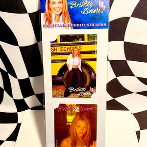 May include: Collectible photo stickers featuring images of Britney Spears. The stickers are on a white card with a blue header that includes the text "Britney Spears" and a butterfly graphic. The stickers show different photos of Britney Spears.