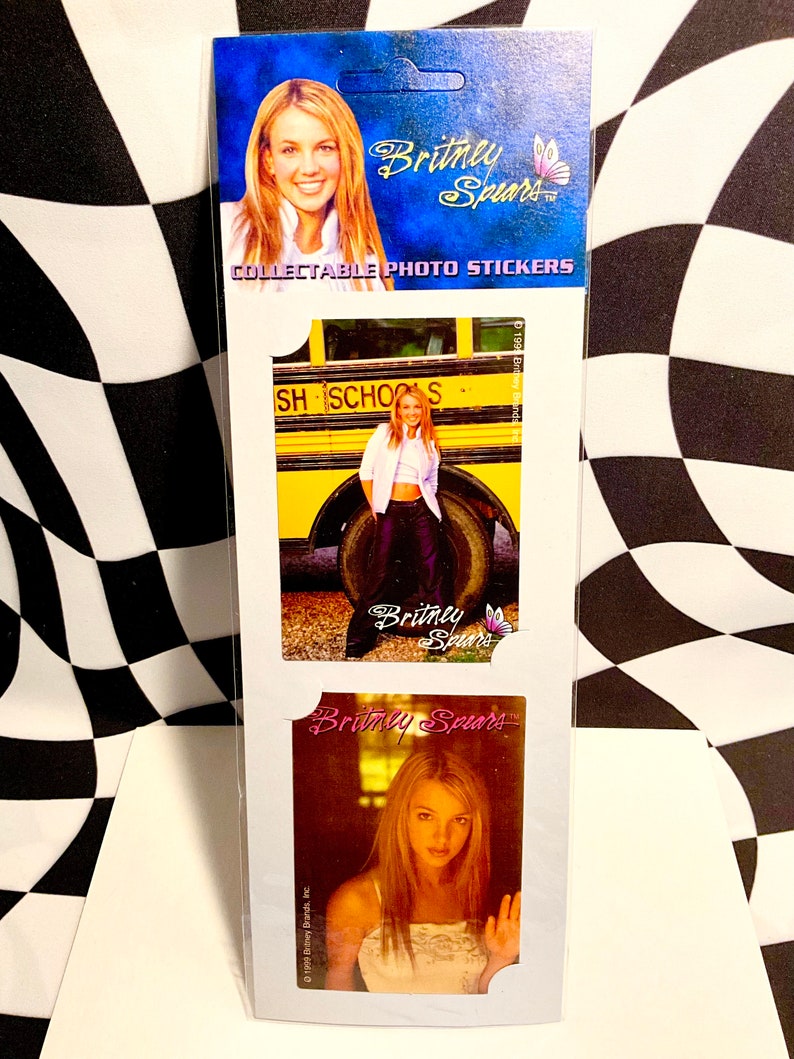 May include: Collectible photo stickers featuring images of Britney Spears. The stickers are on a white card with a blue header that includes the text "Britney Spears" and a butterfly graphic. The stickers show different photos of Britney Spears.