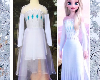 May include: A white dress with a sheer overlay and a blue diamond pattern on the bodice. The dress is similar to the one worn by Elsa in the movie Frozen 2.