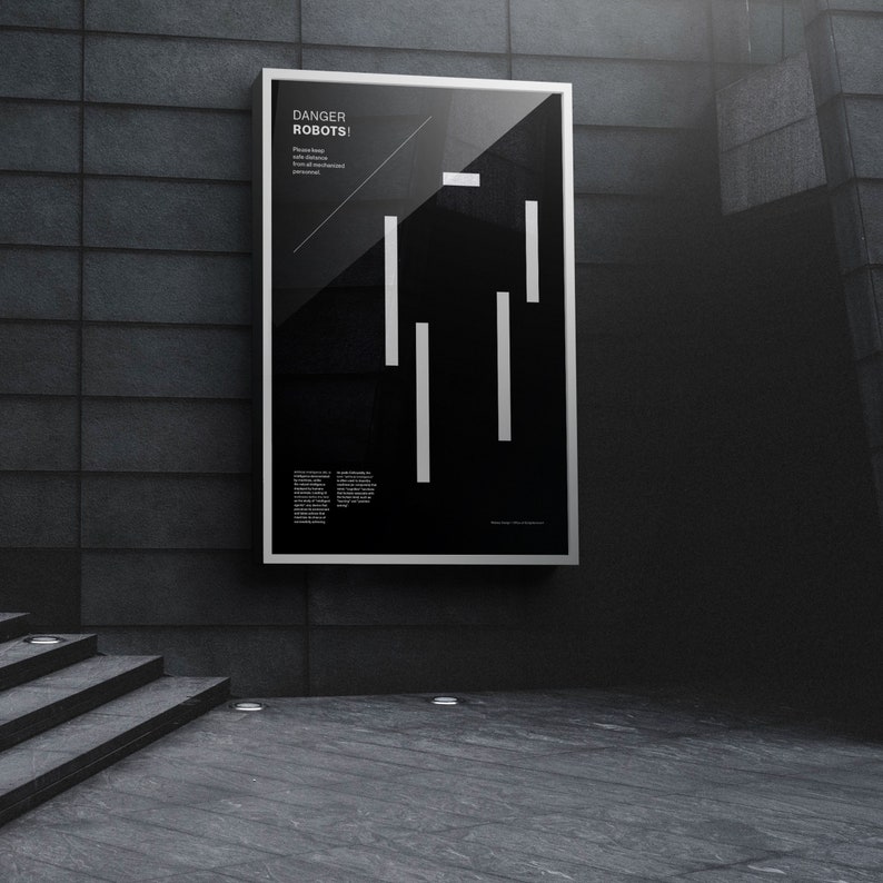 May include: A black and white poster with the text "DANGER ROBOTS!" and a stylized robot figure made of white lines. The poster is framed in a silver frame and is hanging on a gray wall.