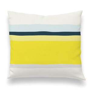 May include: A white pillow with a yellow, light blue, and dark blue striped pattern. The pillow is made of a soft, textured fabric.