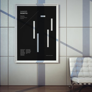 May include: A black and white poster with the text "DANGER ROBOTS!" and a stylized robot figure made of white lines. The poster is framed in white and hanging on a white tiled wall.