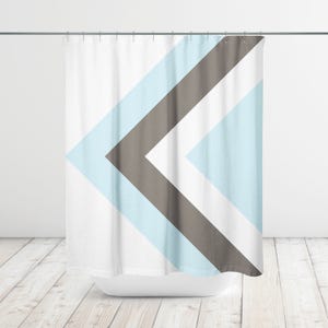 May include: White shower curtain with a geometric design. The design features a large chevron pattern in light blue, gray, and white. The curtain hangs from a silver rod above a white bathtub.