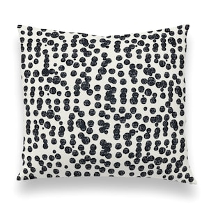 May include: A white throw pillow with a black and white polka dot pattern. The dots are of varying sizes and are slightly textured.