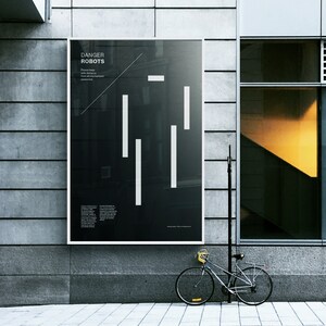 May include: A black and white poster with the text "Danger Robots" and a graphic of white lines on a black background. The poster is mounted on a gray brick wall.