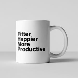 Pode incluir: Uma caneca de cerâmica branca com uma alça curva. A caneca apresenta o texto preto "Fitter, Happier, More, Productive" empilhado verticalmente. A caneca está sobre um fundo branco liso.