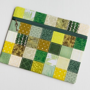 May include: A rectangular patchwork pouch with a zip closure. The design features squares in shades of green and yellow, with leaf and dot patterns. A dark green zip runs across the top, with a key charm. The pouch is made of fabric.