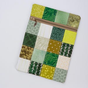 Może przedstawiać: Prostokątna kosmetyczka na zamek błyskawiczny w stylu patchwork. Projekt przedstawia siatkę kwadratów w różnych odcieniach zieleni, żółci i kremu, z różnymi wzorami. Brązowy zamek błyskawiczny przebiega przez górę. Kosmetyczka jest prawdopodobnie używana do przechowywania drobnych przedmiotów.