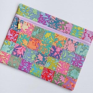 Könnte beinhalten: Bunter Patchwork-Reißverschlusspouch mit floralem Muster in Rosa, Lila, Orange und Türkis. Die Tasche hat einen lila Reißverschluss und eine gelbe Quaste. Das Design besteht aus mehreren Quadraten. Die Tasche ist ca. 30 cm breit.