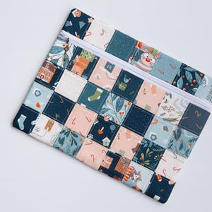 Könnte beinhalten: Ein gesteppter Beutel mit einem Patchwork-Design mit Weihnachtsmotiven. Die Quadrate sind in den Farbtönen Marineblau, Türkis und Pfirsich gehalten und zeigen Bilder von Häusern, Strümpfen und Schneemännern. Er hat einen weißen Reißverschluss.