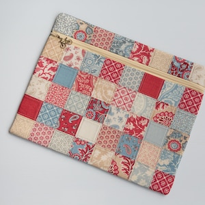 May include: A patchwork zipped pouch with a variety of patterned fabric squares in red, blue, and cream. The pouch has a gold-coloured zip and a decorative zip pull. The design is reminiscent of a quilt.