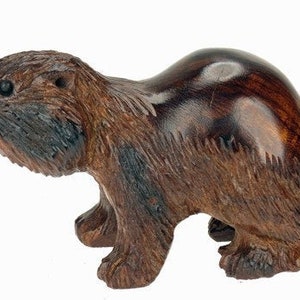 Puede incluir: Una figurita de castor de madera tallada a mano con un acabado marrón oscuro. El castor está de pie sobre sus cuatro patas con la cola detrás.