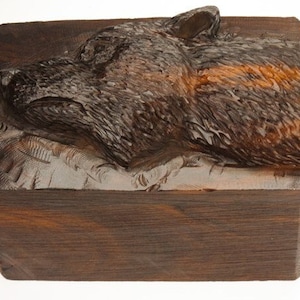 Peut inclure: Une boîte en bois avec une tête de loup sculptée sur le couvercle. La boîte est en bois foncé avec une finition naturelle.