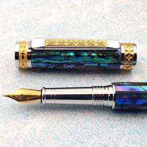 Op de afbeelding: Een blauwe en groene abalone-schelp vulpen met een gouden rand en een gouden penpunt. De pen is gesloten en de dop is eraf.