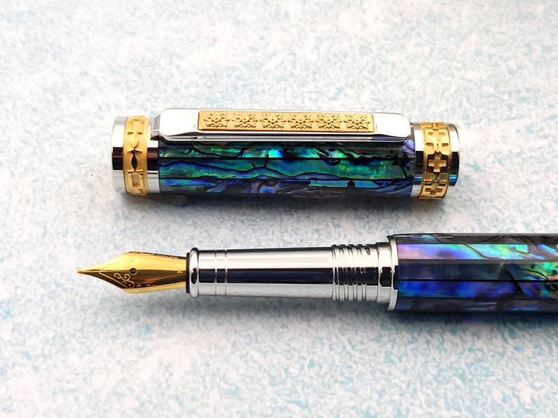 Op de afbeelding: Een blauwe en groene abalone-schelp vulpen met een gouden rand en een gouden penpunt. De pen is gesloten en de dop is eraf.