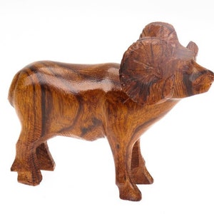 Puede incluir: Una escultura de madera de un carnero con grandes cuernos. La escultura está hecha de madera marrón oscura con un acabado pulido.