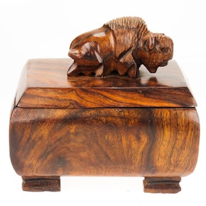 Peut inclure: Une boîte en bois avec un buffle sculpté sur le couvercle. La boîte est en bois foncé avec un beau grain.