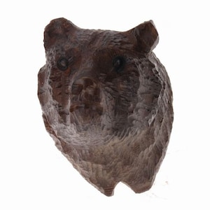May include: A carved wooden bear head sculpture with a detailed, textured surface. The bear's eyes are carved into the wood and the sculpture is painted in a dark brown color.