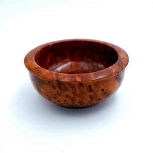 May include: A small, round wooden bowl with a rich brown color and a natural wood grain pattern. The bowl is made of a single piece of wood and has a smooth, polished finish.