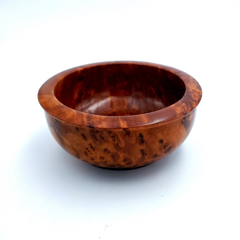 May include: A small, round wooden bowl with a rich brown color and a natural wood grain pattern. The bowl is made of a single piece of wood and has a smooth, polished finish.