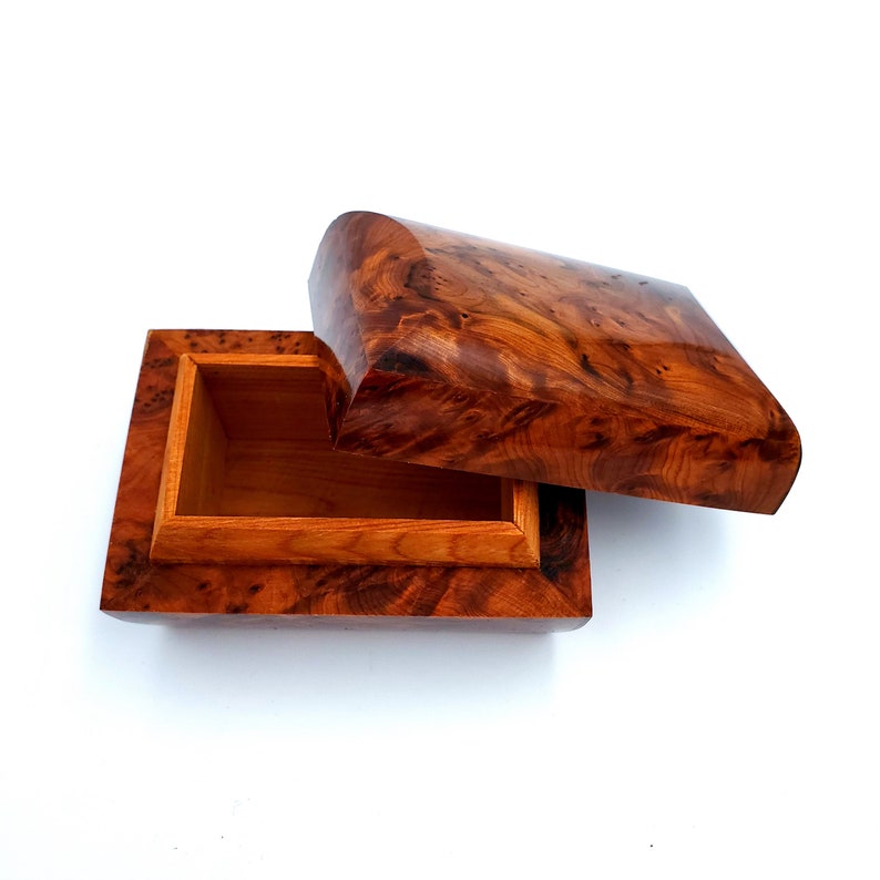 May include: A wooden box with a lid that is open. The box is made of a dark wood with a natural grain pattern. The inside of the box is lined with a lighter wood.