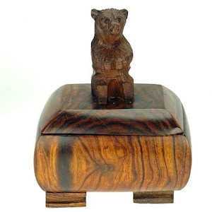Peut inclure: Une boîte en bois avec un ours sculpté sur le dessus. La boîte est en bois foncé avec un beau grain. L'ours est assis droit, ses pattes reposant sur le couvercle de la boîte.