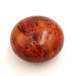 May include: A round wooden box with a natural wood grain finish. The box is made of a reddish-brown wood with a unique pattern of dark brown spots.