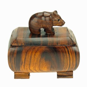Peut inclure: Une boîte en bois avec un ours sculpté sur le couvercle. La boîte est en bois foncé avec un beau grain. Elle a une forme rectangulaire aux bords arrondis et repose sur quatre petits pieds.