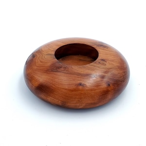 May include: A round wooden bowl with a smooth, reddish-brown finish. The bowl has a deep, circular indentation in the center.