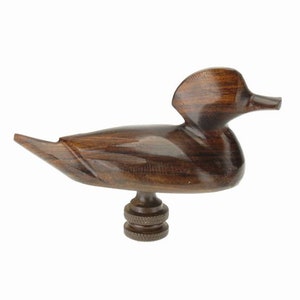 May include: A wooden duck lamp finial with a dark brown finish. The duck is carved in a realistic style and has a detailed head and body.