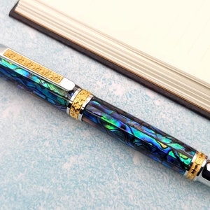 Op de afbeelding: Een blauwe en groene pen met gouden accenten en een zilveren dop. De pen is gemaakt van abalone-schelp en heeft een uniek, ingewikkeld ontwerp.