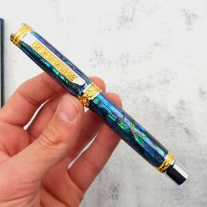 Op de afbeelding: Een blauwe en groene pen met gouden accenten en een zilveren punt. De pen is gemaakt van abalone-schelp en heeft een textuurontwerp.