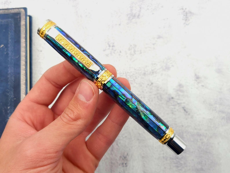 Op de afbeelding: Een blauwe en groene pen met gouden accenten en een zilveren punt. De pen is gemaakt van abalone-schelp en heeft een textuurontwerp.