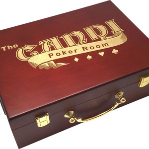 May include: A wooden poker set case with a dark red finish. The case features gold-colored hardware, including a handle, latches, and a decorative emblem. The text "The GANDI Poker Room" is displayed in gold lettering on the lid, along with suit symbols.