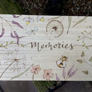 May include: A wooden box with a woodburned design of flowers, leaves, and a bee. The box is labeled "Memories".