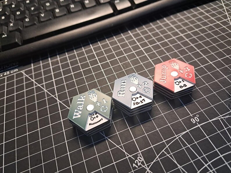 Pode incluir: Tr&ecirc;s pe&ccedil;as de jogo hexagonais com diferentes op&ccedil;&otilde;es de movimento: "Caminhar", "Correr" e "Saltar". Cada pe&ccedil;a tem uma cor diferente: verde, azul e vermelho. As pe&ccedil;as t&ecirc;m n&uacute;meros e s&iacute;mbolos.
