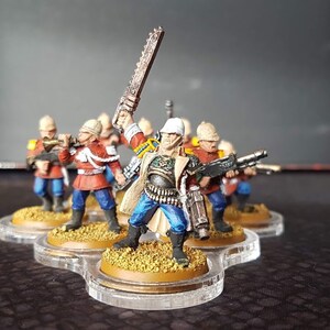 Może przedstawiać: Grupa sześciu pomalowanych miniaturek w kolorze czerwonym, niebieskim i białym, trzymających r&oacute;żne bronie. Figurki stoją na okrągłych podstawach i są ułożone w k&oacute;łko.