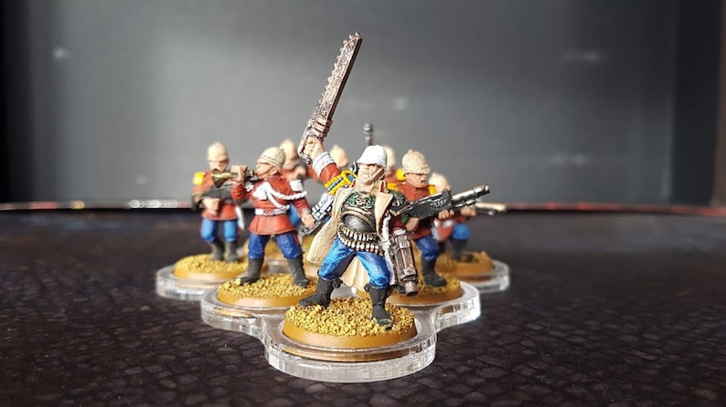 Może przedstawiać: Grupa sześciu pomalowanych miniaturek w kolorze czerwonym, niebieskim i białym, trzymających r&oacute;żne bronie. Figurki stoją na okrągłych podstawach i są ułożone w k&oacute;łko.