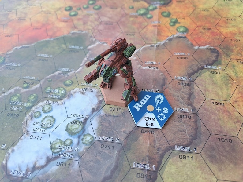 Puede incluir: Una figura de robot en miniatura de color marr&oacute;n y verde con una pistola, de pie en un tablero de juego hexagonal con una ficha azul y blanca que dice "Run" y tiene un s&iacute;mbolo de m&aacute;s dos y un s&iacute;mbolo de m&aacute;s dos con 5-6 escrito debajo. El tablero tiene n&uacute;meros y texto que dice "Nivel 1" y "Nivel 2".