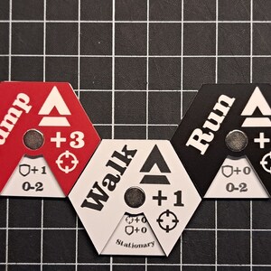Puede incluir: Tres piezas de juego hexagonales con diferentes opciones de movimiento: "Saltar" (rojo), "Caminar" (blanco) y "Correr" (negro). Cada pieza tiene un icono de escudo, un icono de objetivo y un n&uacute;mero que indica la velocidad de movimiento.