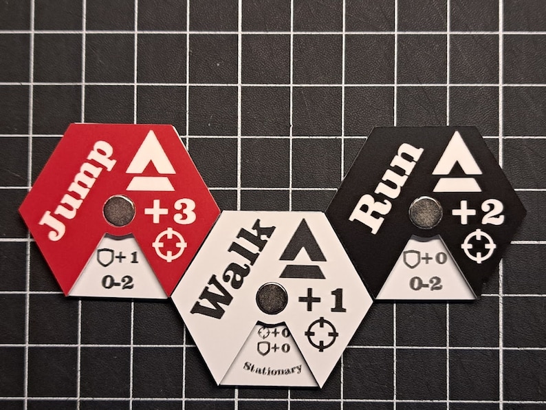 Puede incluir: Tres piezas de juego hexagonales con diferentes opciones de movimiento: "Saltar" (rojo), "Caminar" (blanco) y "Correr" (negro). Cada pieza tiene un icono de escudo, un icono de objetivo y un n&uacute;mero que indica la velocidad de movimiento.