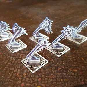 May include: Five clear acrylic miniature weapon bases with different weapon designs. The bases are square and have a black and white design with the words "Spectral" and "Weapon" printed on them.
