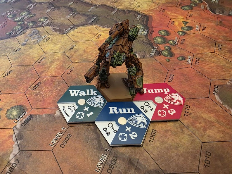 Puede incluir: Una figura de robot en miniatura de color verde, marr&oacute;n y gris con una gran pistola. La figura est&aacute; de pie sobre una base marr&oacute;n. Tres piezas de juego hexagonales est&aacute;n delante de la figura. Las piezas son azules, verdes y rojas. La pieza azul dice "Run" y tiene un signo m&aacute;s con el n&uacute;mero 2. La pieza verde dice "Walk" y tiene un signo m&aacute;s con el n&uacute;mero 1. La pieza roja dice "Jump" y tiene un signo m&aacute;s con el n&uacute;mero 3.