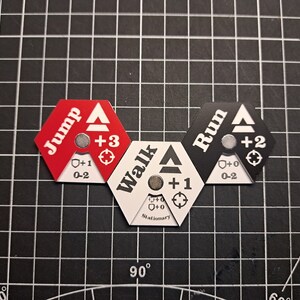 Puede incluir: Tres piezas de juego hexagonales con diferentes opciones de movimiento: "Jump" en rojo, "Walk" en blanco y "Run" en negro. Cada pieza tiene una flecha blanca, un n&uacute;mero y un s&iacute;mbolo.
