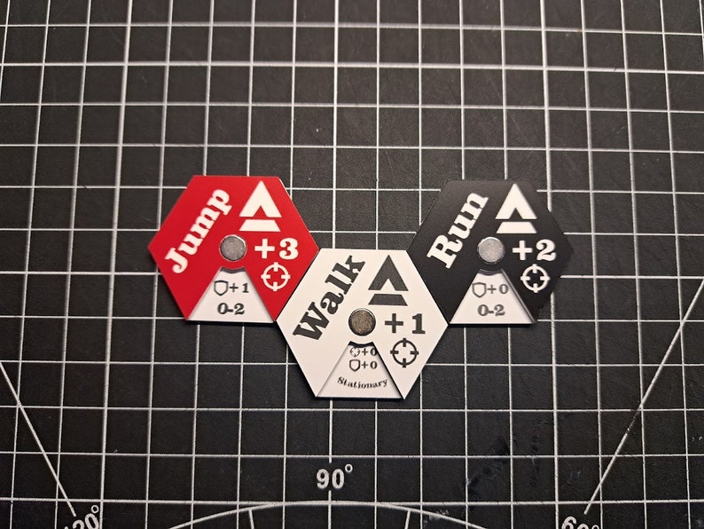 Puede incluir: Tres piezas de juego hexagonales con diferentes opciones de movimiento: "Jump" en rojo, "Walk" en blanco y "Run" en negro. Cada pieza tiene una flecha blanca, un n&uacute;mero y un s&iacute;mbolo.