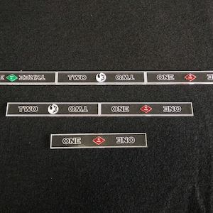 May include: A set of black acrylic tiles with white text and symbols. The tiles read "THREE", "TWO", "ONE", and "ZERO".