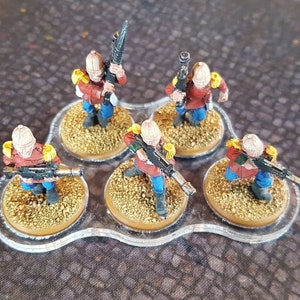 Może przedstawiać: Sześć miniaturowych figurek żołnierzy pomalowanych na czerwono, niebiesko i ż&oacute;łto, trzymających karabiny i stojących na okrągłych podstawach. Figurki są ułożone w k&oacute;łko na przezroczystej plastikowej podstawie.