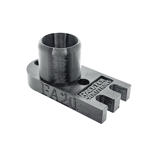 Może przedstawiać: Czarny, drukowany w 3D element z tworzywa sztucznego z cylindryczną górą i prostokątną podstawą z trzema zębami. Na podstawie znajduje się tekst "FA20" i "RAZTEK SOLUTIONS". Ten element jest przeznaczony do określonej funkcji mechanicznej.