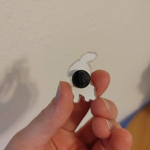 May include: White enamel pin of a rabbit with a black pin back.